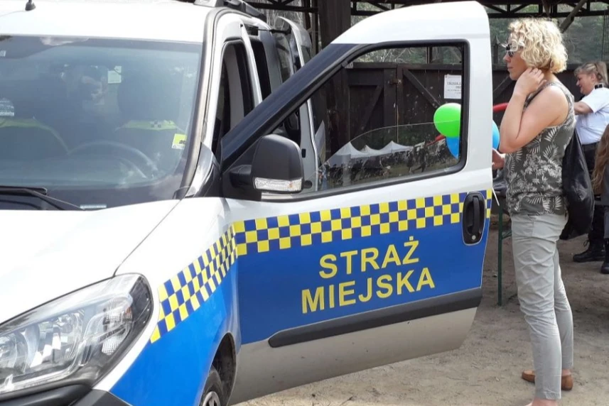 Kobieta stojąca przy samochodzie straży miejskiej.
