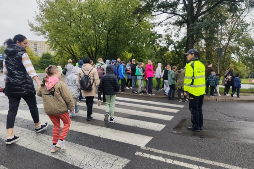 Grupa dzieci przechodzi przez ulicę  w asyście Straży Miejskiej.