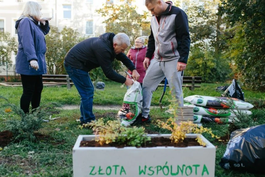 Grupa ludzi sadzi rośliny na osiedlowym skwerze.