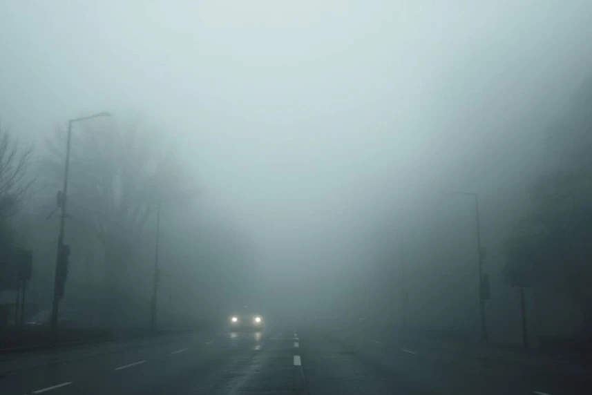 Zamglona ulica miasta. Na zdjęciu widać światła samochodu.