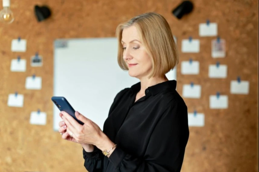Kobieta ubrana w czarną bluzkę trzyma w dłoniach telefon komórkowy.