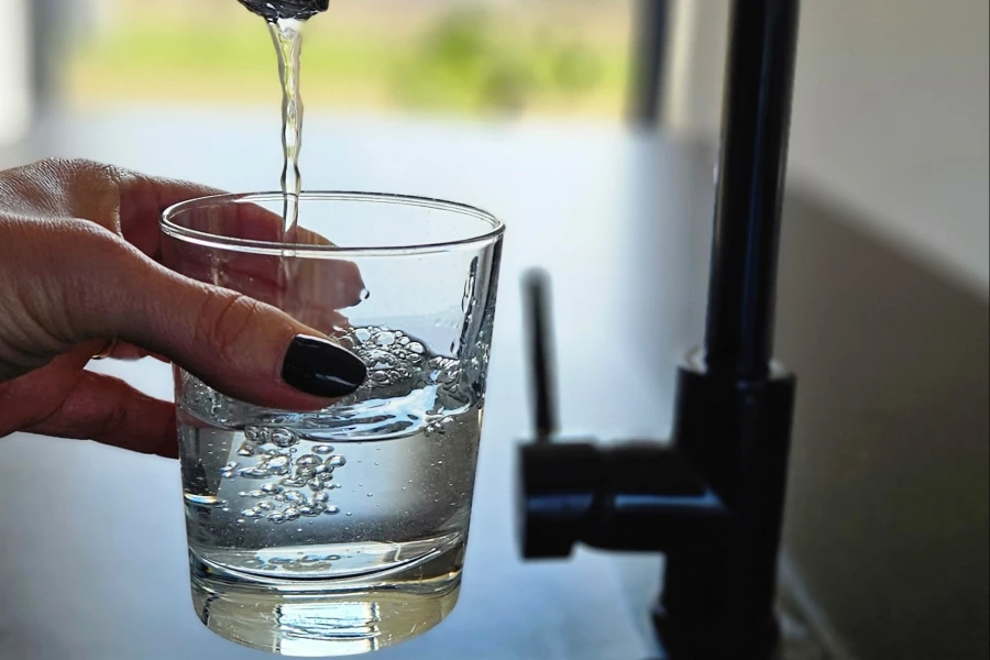 Dłoń trzymająca napełniającą się szklankę wody.