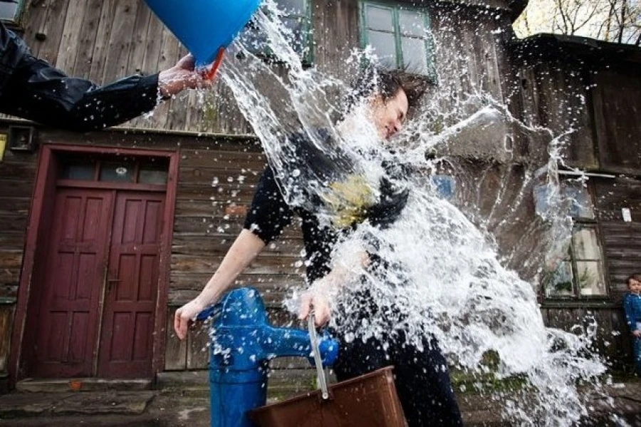 Moment wylania wody z niebieskiego wiadra na osobę przy niebieskiej pompie wodnej.
