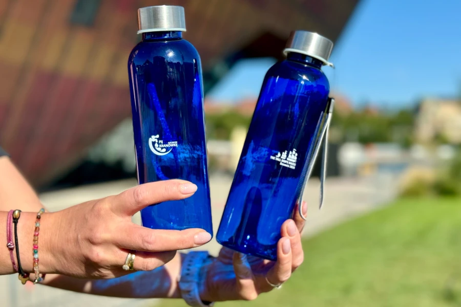 Dwie granatowe butelki z woda trzymane w dłoniach.