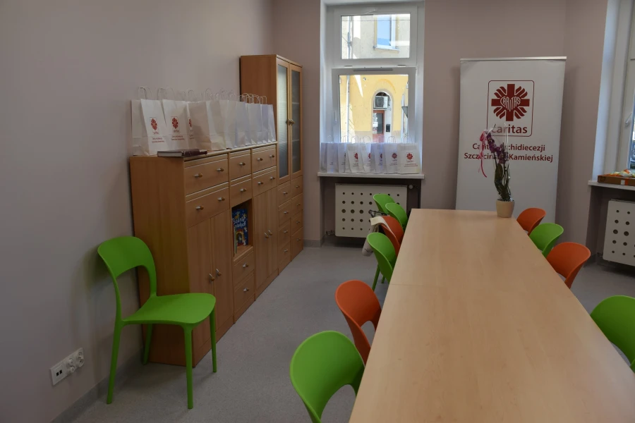 Pokój świetlicy z kolorowymi krzesłami, regałem i ławką.