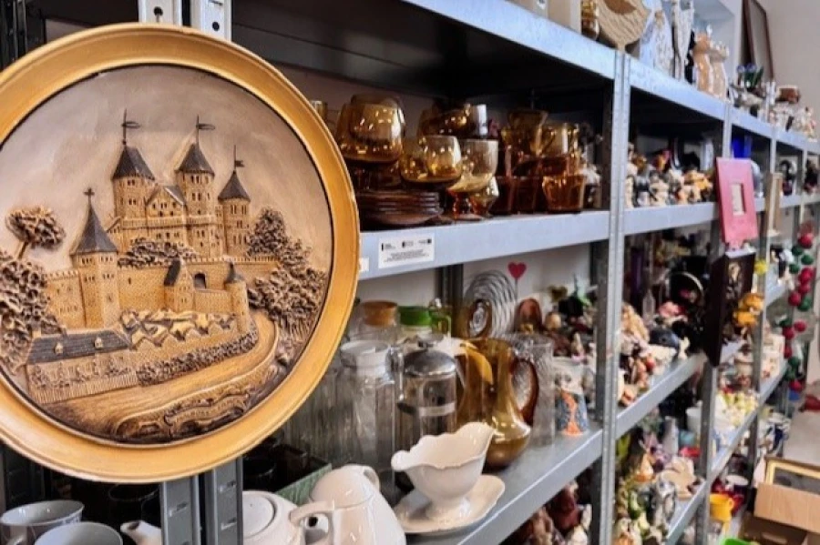 Półka wystawowa z filiżankami, kubkami. Na pierwszym planie okrągły obraz.