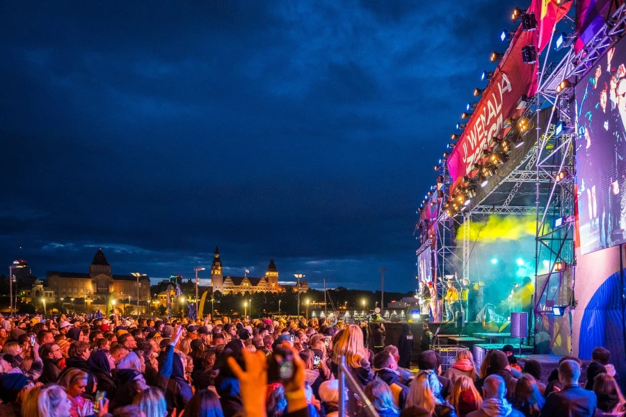 Tłum ludzi zgromadzonych pod sceną. W tle ciemne niebo i zabytki Szczecina.