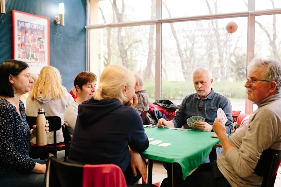 Grupa osób siedząca przy stoliku i grająca w brydża.