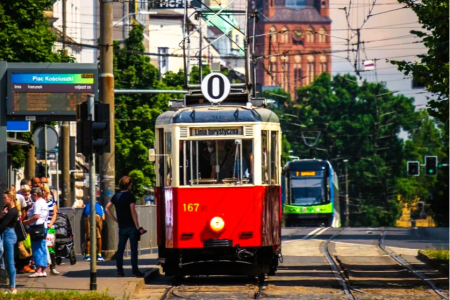 Czerwony tramwaj turystyczny linii 0. Z lewej strony przystanek z grupą ludzi. Czerwony tramwaj turystyczny linii 0. Z lewej strony przystanek z grupą ludzi.